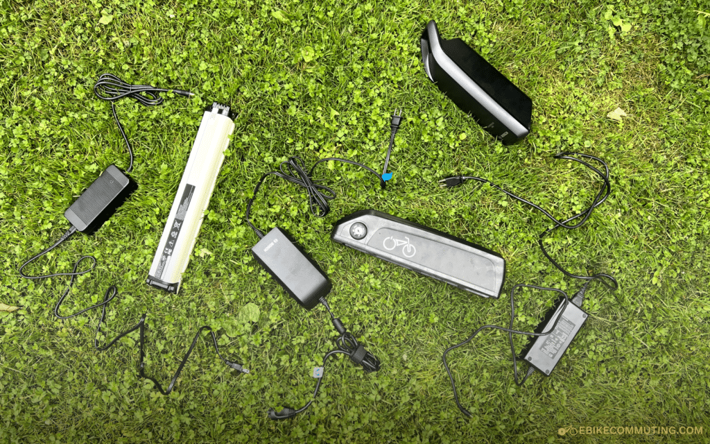 multiple e-bike batteries and chargers laying on grass