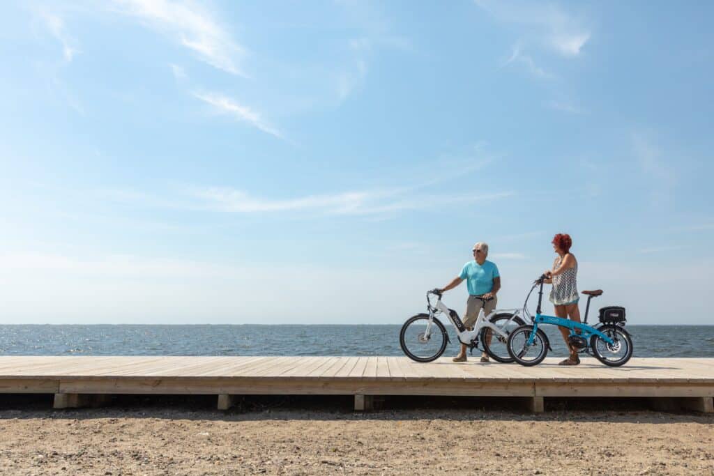 Man and woman standing next to e-bikes on boardwalk above sandy beach