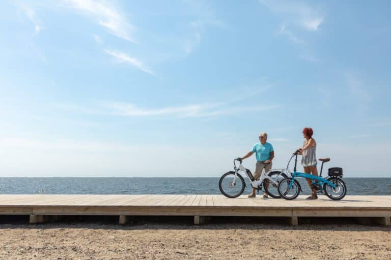 Man and woman standing next to e-bikes on boardwalk above sandy beach